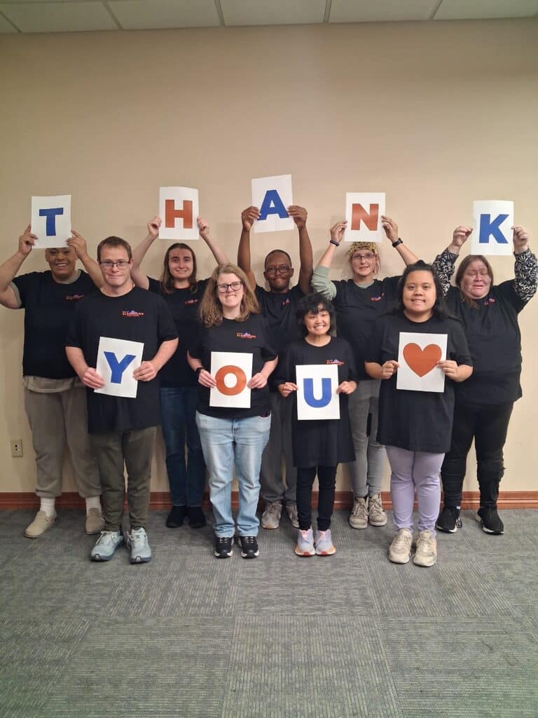 RiseUP participants and community members in Colorado Springs, Colorado, wearing RiseUP Elevation Challenge shirts and holding signs that spell “THANK YOU” with a heart, celebrating inclusion, community support, and services for individuals with intellectual and developmental disabilities and neurodiversity.